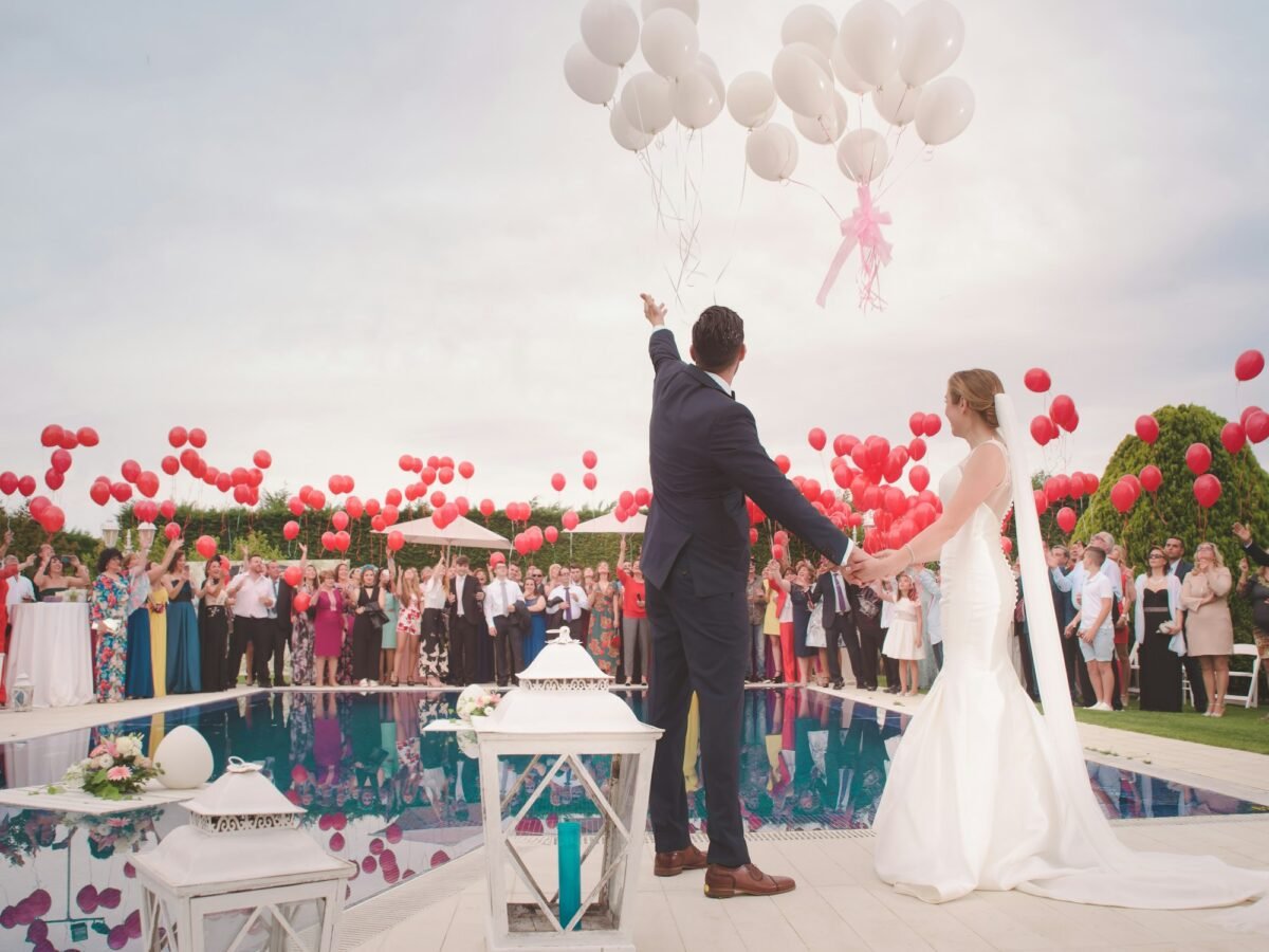 Bride and groom at an outdoor wedding with red balloons
