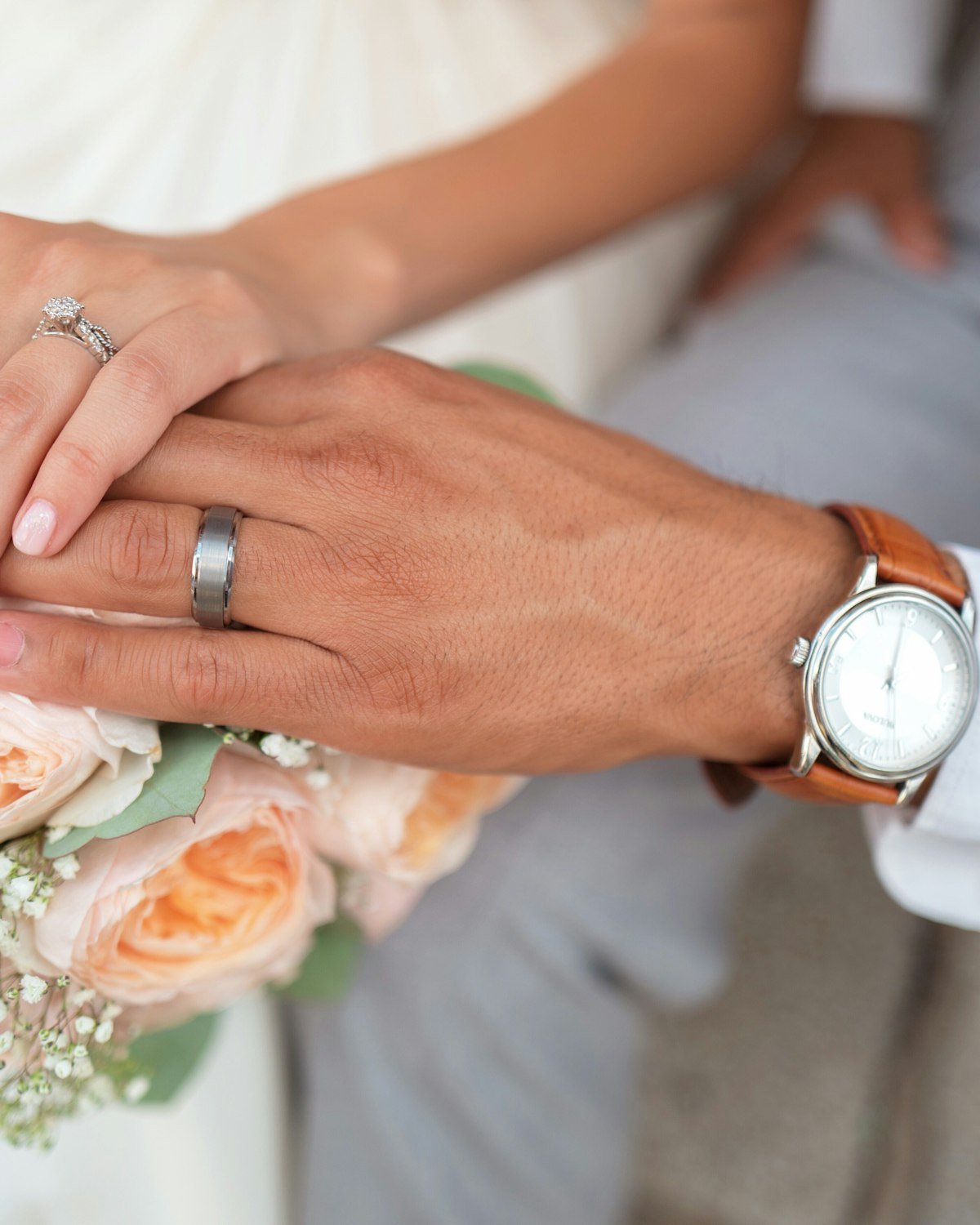 Bride and groom holding hands with wedding rings and a bouquet
